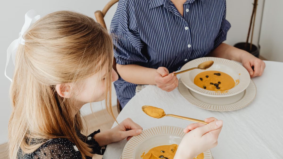 Mother and daughter enjoying a cozy indoor meal with delicious pumpkin soup.