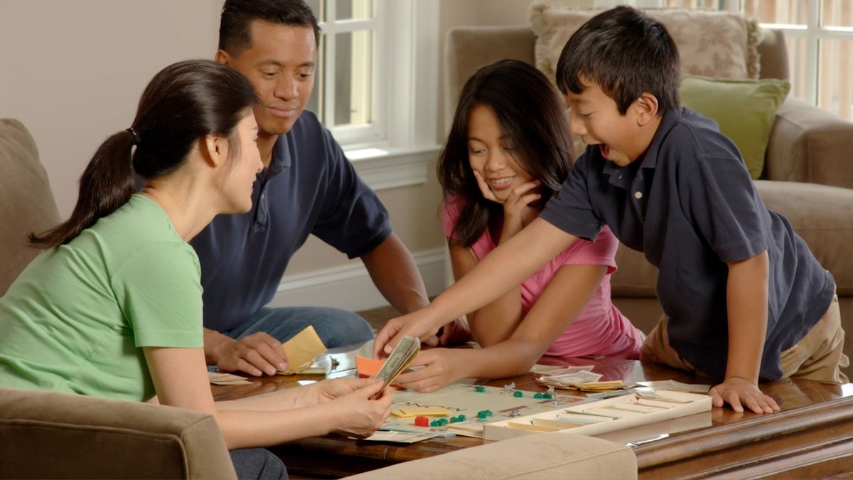 Family Playing A Board Game. An Asian family (adult male and female and two adolescents, male and female) sitting around a coffee table playing a board game. Photographer Bill Branson